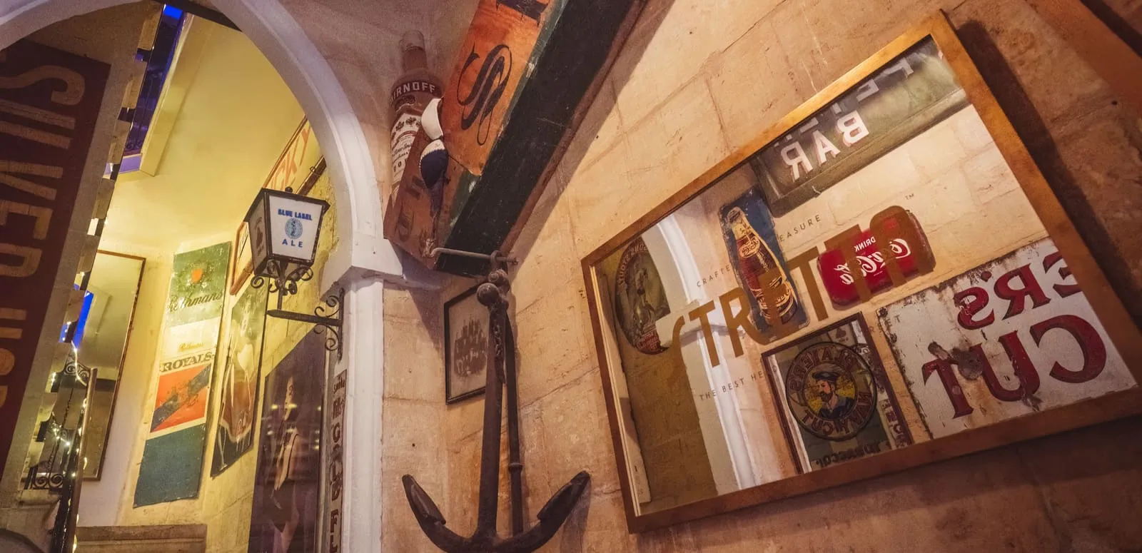 The bar interior: an anchor and framed vintage advertising signs covering the stone walls.