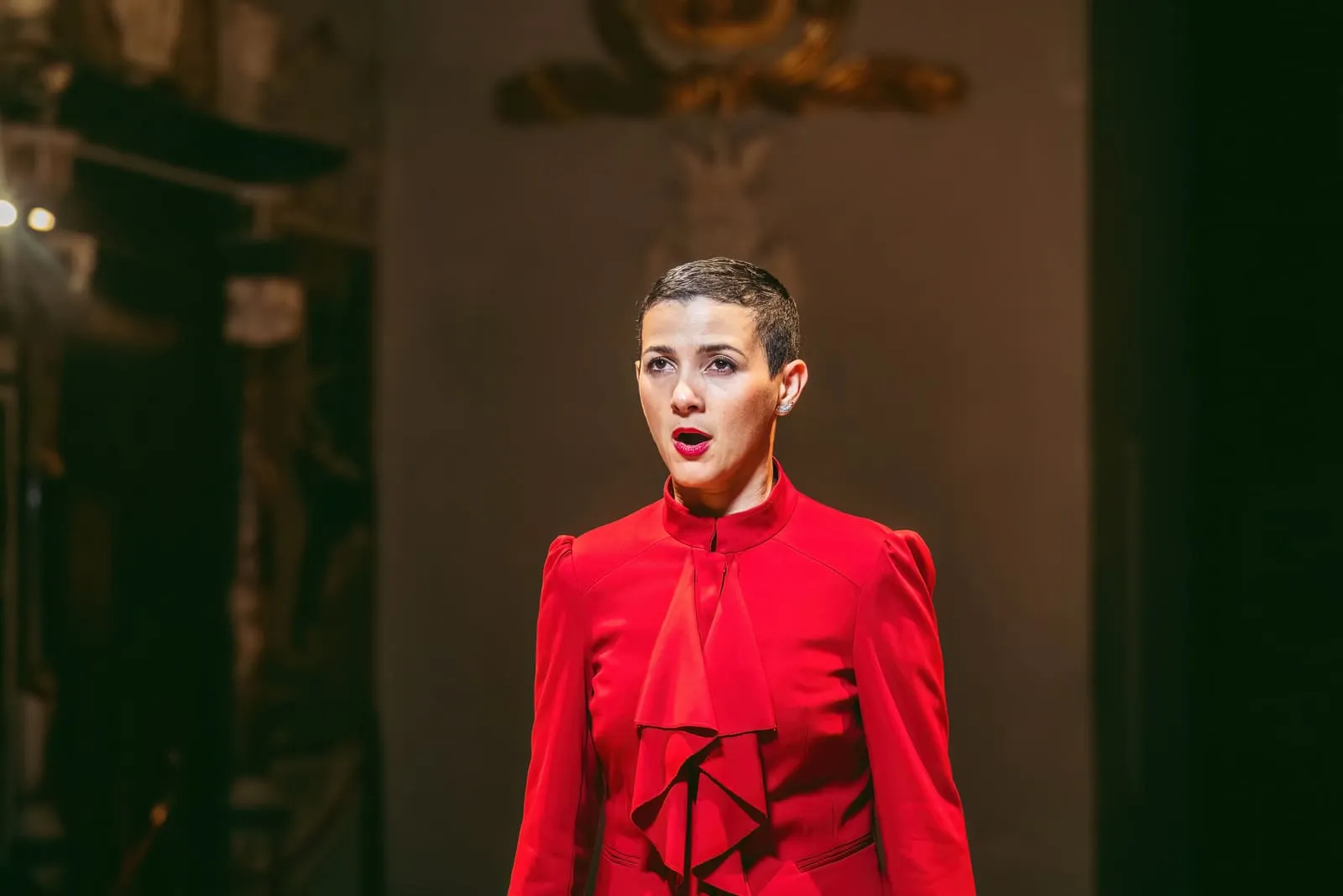 A soprano in red singing in the Oratory, lit against the darkness.