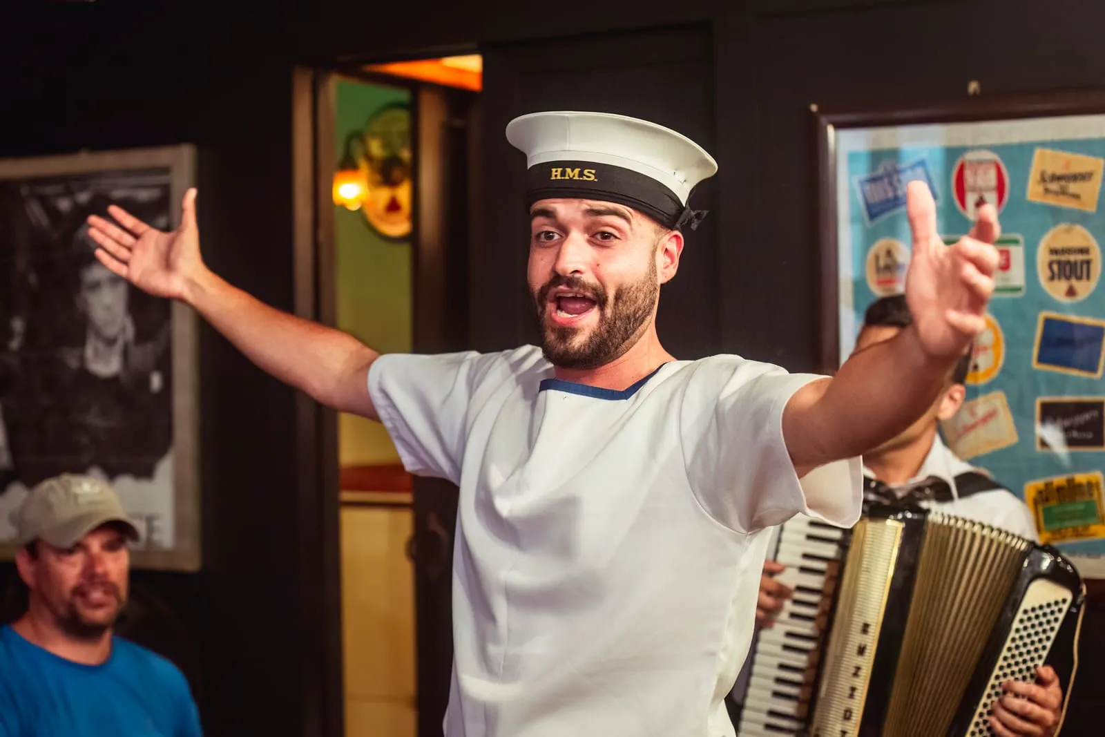 Duminku the sailor, in whites and a cap, singing with his arms thrown wide.