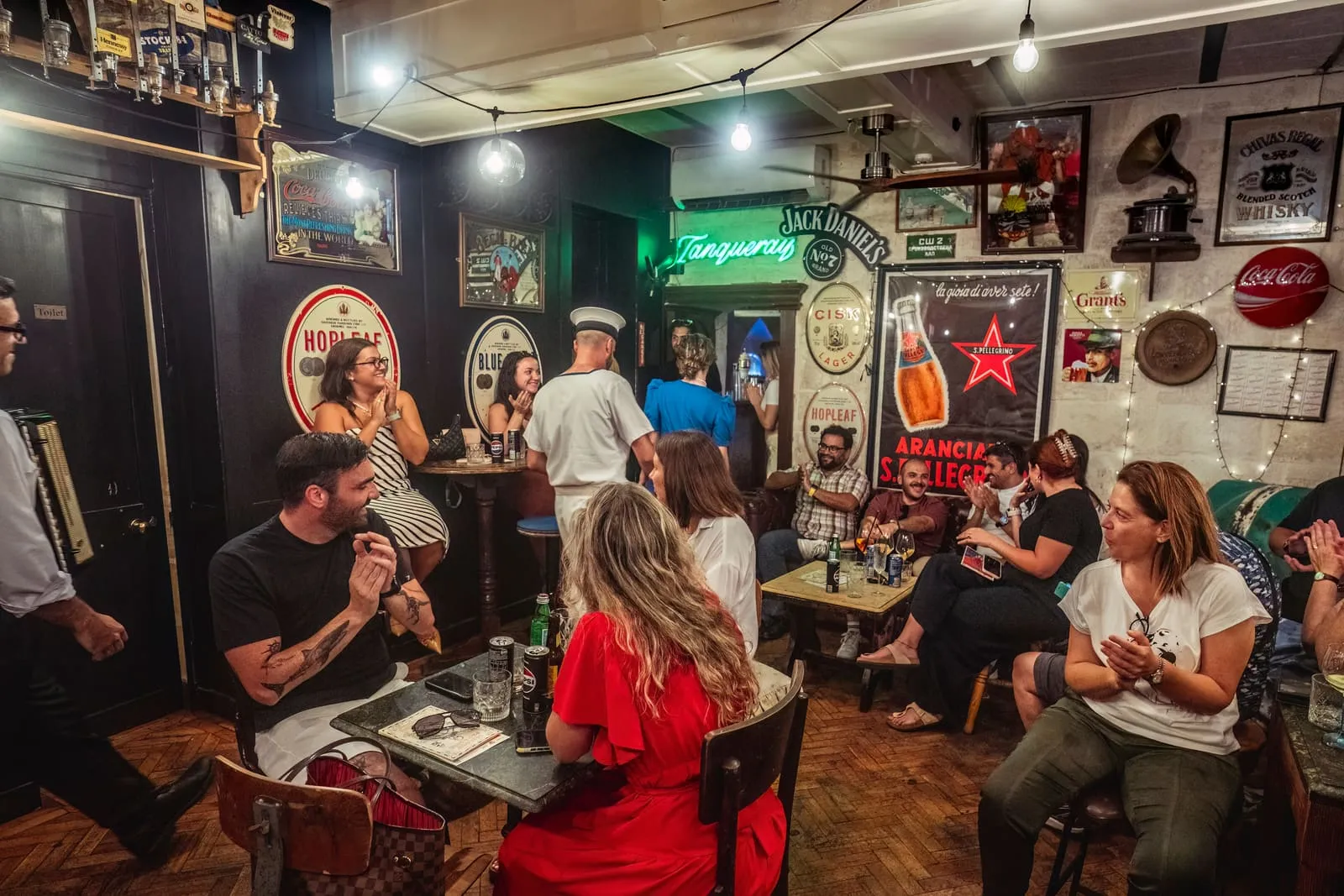 Guests seated with drinks around the small bar as the performance plays out among them.